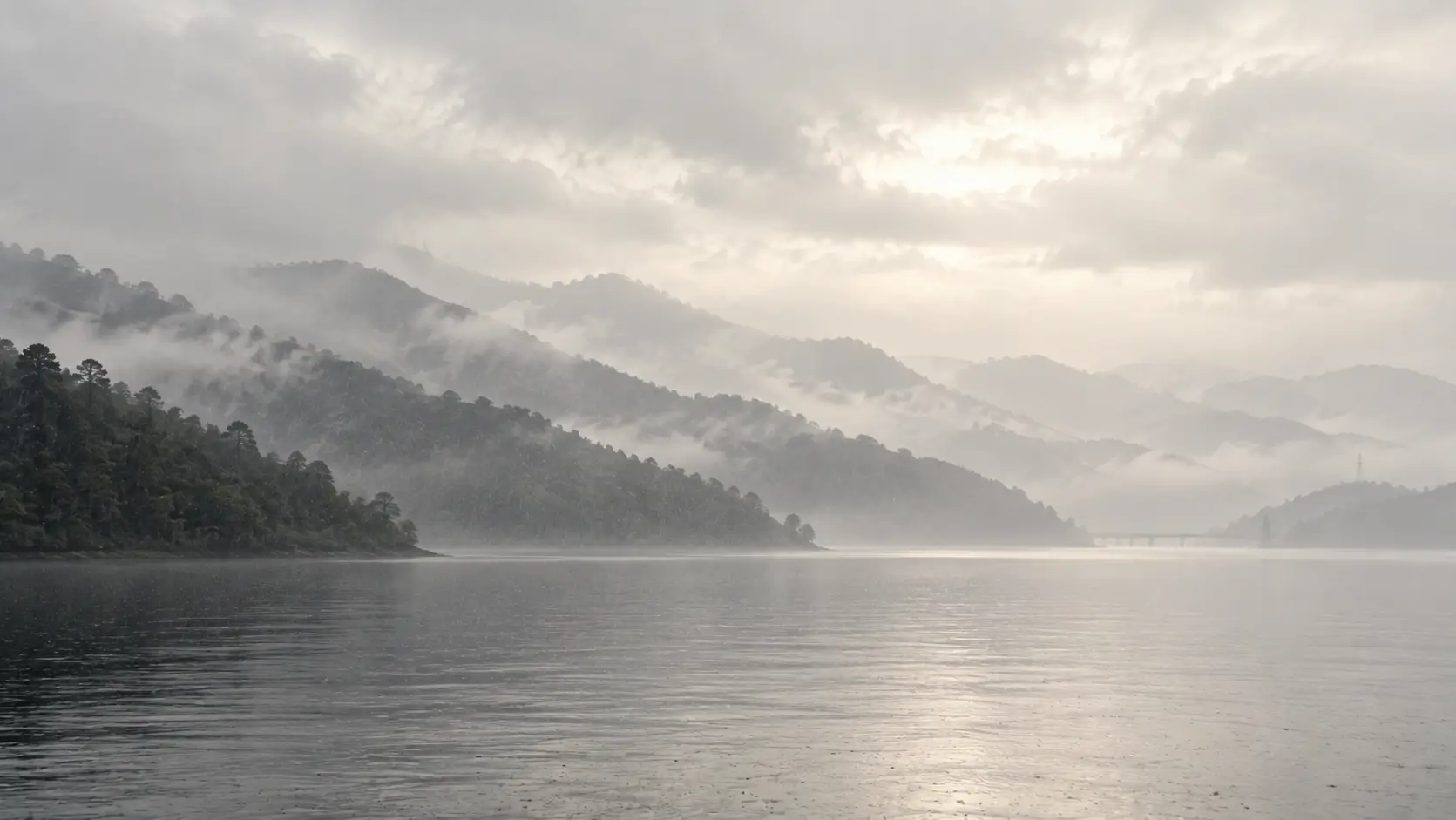 Layered forested ridges dissolving into rain above still silver water